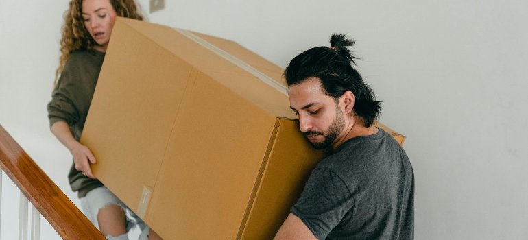 A man and a woman carry a box, showing teamwork and planning—key steps in how to make moving less stressful.