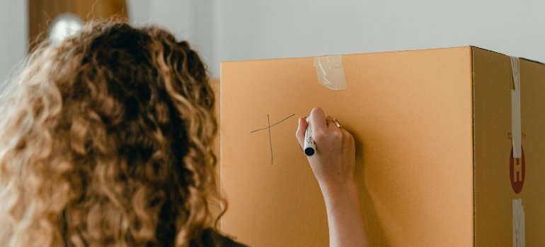 girl marks a box during a move like of the ways how to make moving less stressful