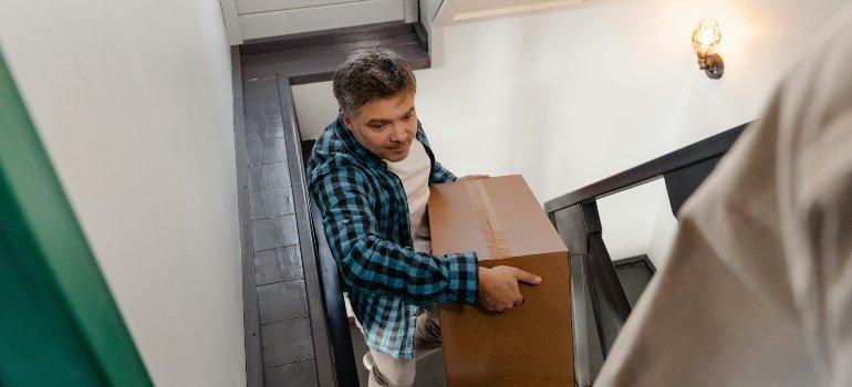 Person struggling to carry a large box up narrow stairs during a move.