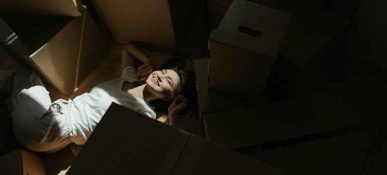 Woman in white dress shirt lying on a brown cardboard box, relaxing after a successful move with movers Canoga Park.