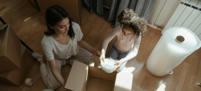 Woman in Gray Shirt Sitting on Floor Beside Girl in White Shirt