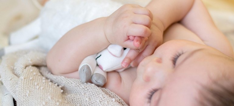 Baby lying on a blanket holding a toy, moving with a newborn in a new home environment