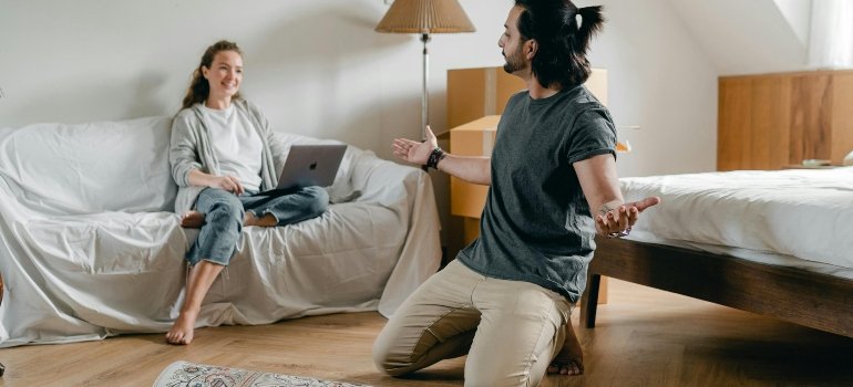 Happy woman with laptop looking at ethnic man with carpet