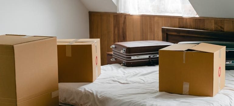 Carton boxes and suitcases placed on bed in empty light room