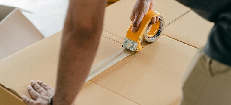 Crop faceless man packing box with scotch tape