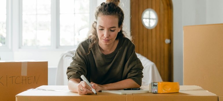 Woman labeling moving boxes at home to avoid common moving mistakes during relocation