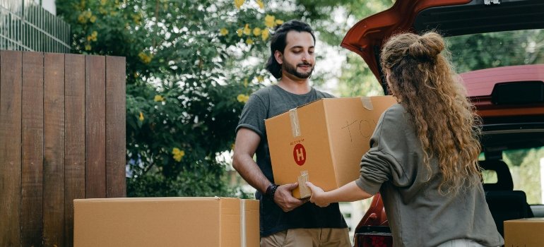 Couple passing a carton box to each other while packing a car, showing why movers Chatsworth CA can simplify the process.
