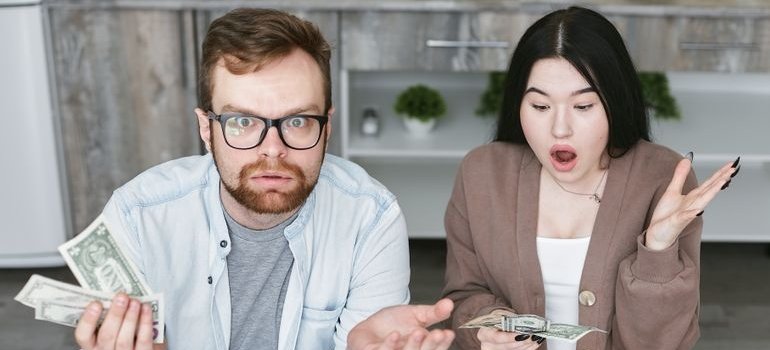 a couple looking surprised while reviewing cash and bills at a kitchen table