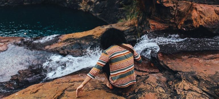 Man in Green and Yellow Stripe Long Sleeve Shirt Sitting on Brown Rocky Mountain