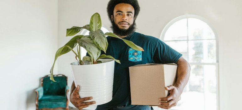 Man holding a brown box and potted plant during relocation with professional movers Tarzana CA.