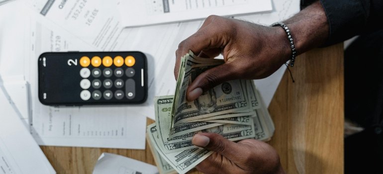 Person counting money on the table next to a calculator and papers, showing budgeting tips for moving out for the first time.