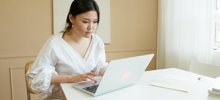 woman in white top using Macbook Air to learn plan a long distance move